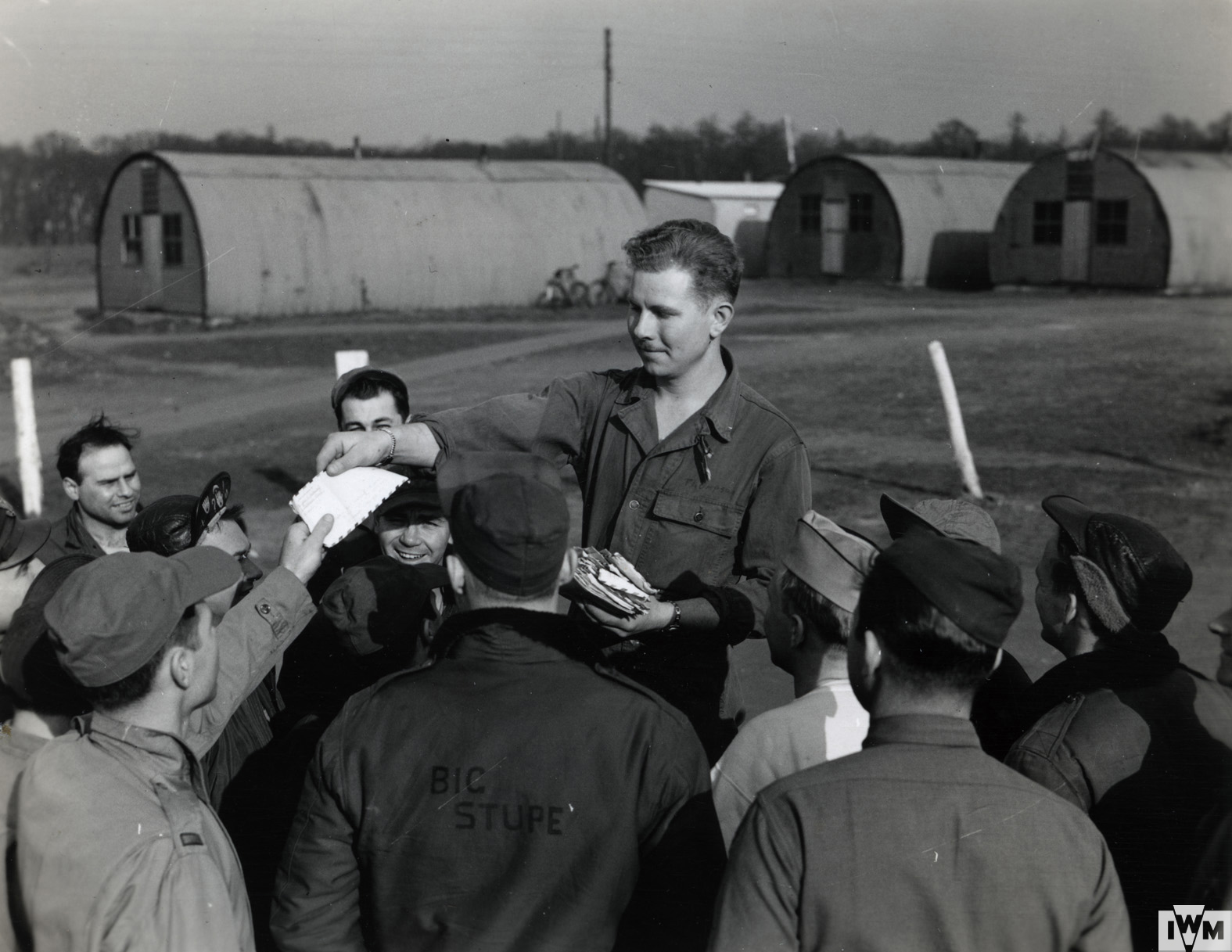 An officer hands out letters from home to US Army Air Force personnel in front of Nissen Huts. Handwritten caption on reverse: 'Letters From Home.'