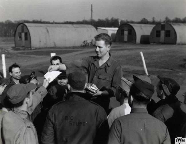 An officer hands out letters from home to US Army Air Force personnel in front of Nissen Huts. Handwritten caption on reverse: 'Letters From Home.'